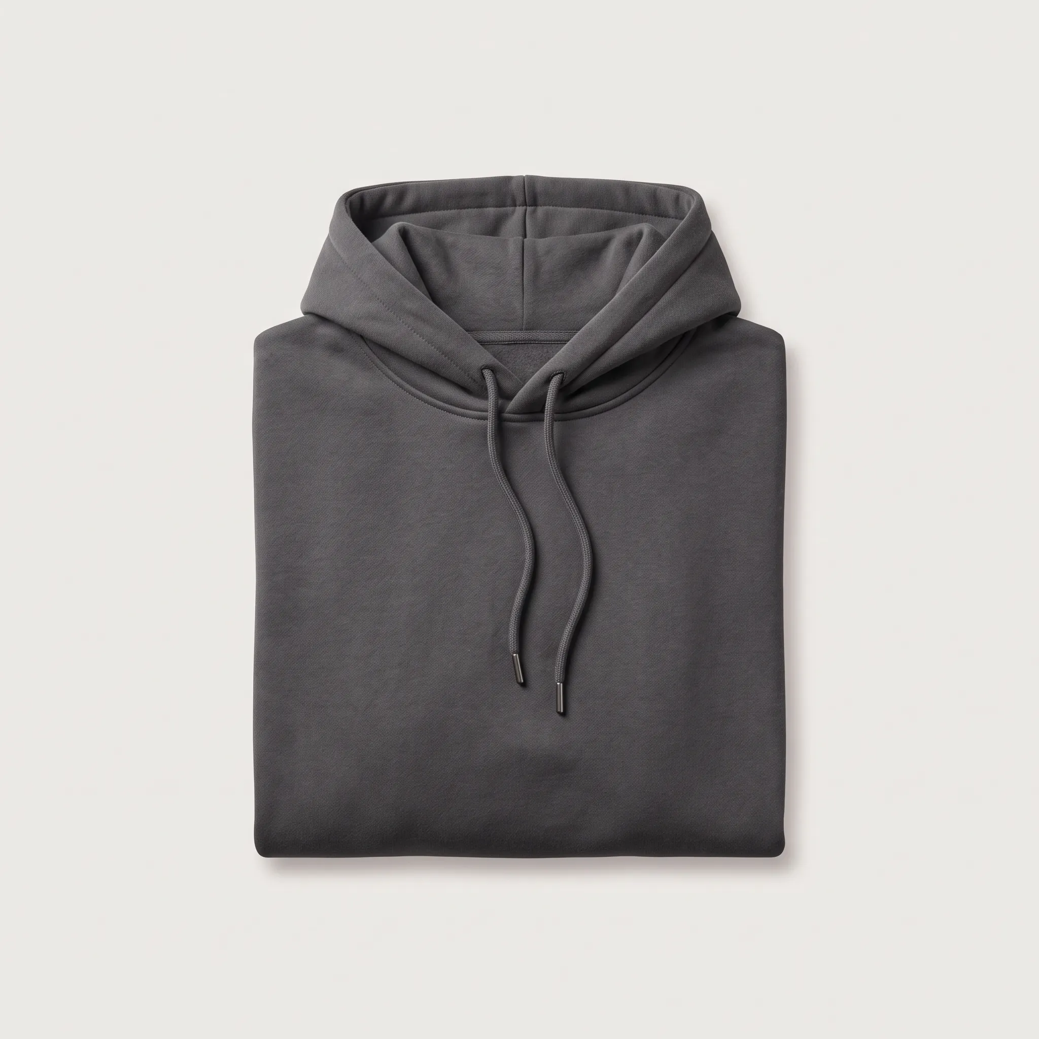 Tampilan rata atas jaket bertopi (hoodie) model pullover berwarna abu-abu tua yang dilipat rapi, menampilkan bagian tudung dan tali serut dengan ujung logam di bagian atas.