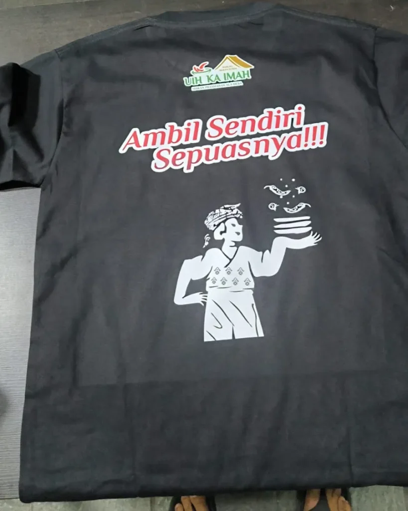Kaos hitam seragam restoran prasmanan bertuliskan "Ambil Sendiri Sepuasnya!!!" dengan logo "Uih Ka Imah" serta ilustrasi koki Sunda membawa tumpukan piring.