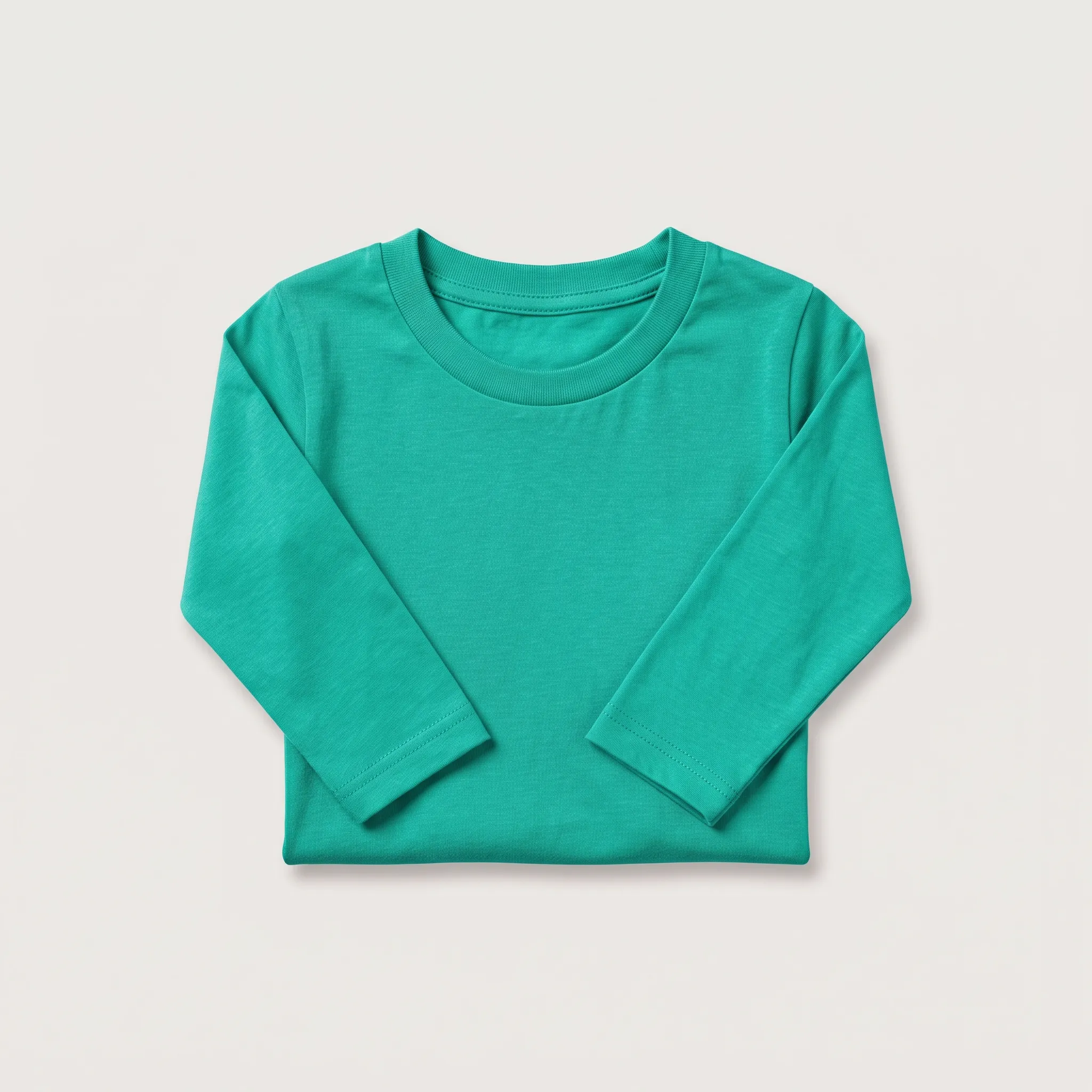 Kaos lengan panjang anak-anak berwarna hijau toska atau teal cerah yang dilipat rapi, menampilkan kerah bulat dan lengan yang ditekuk ke dalam, siap untuk pengemasan.