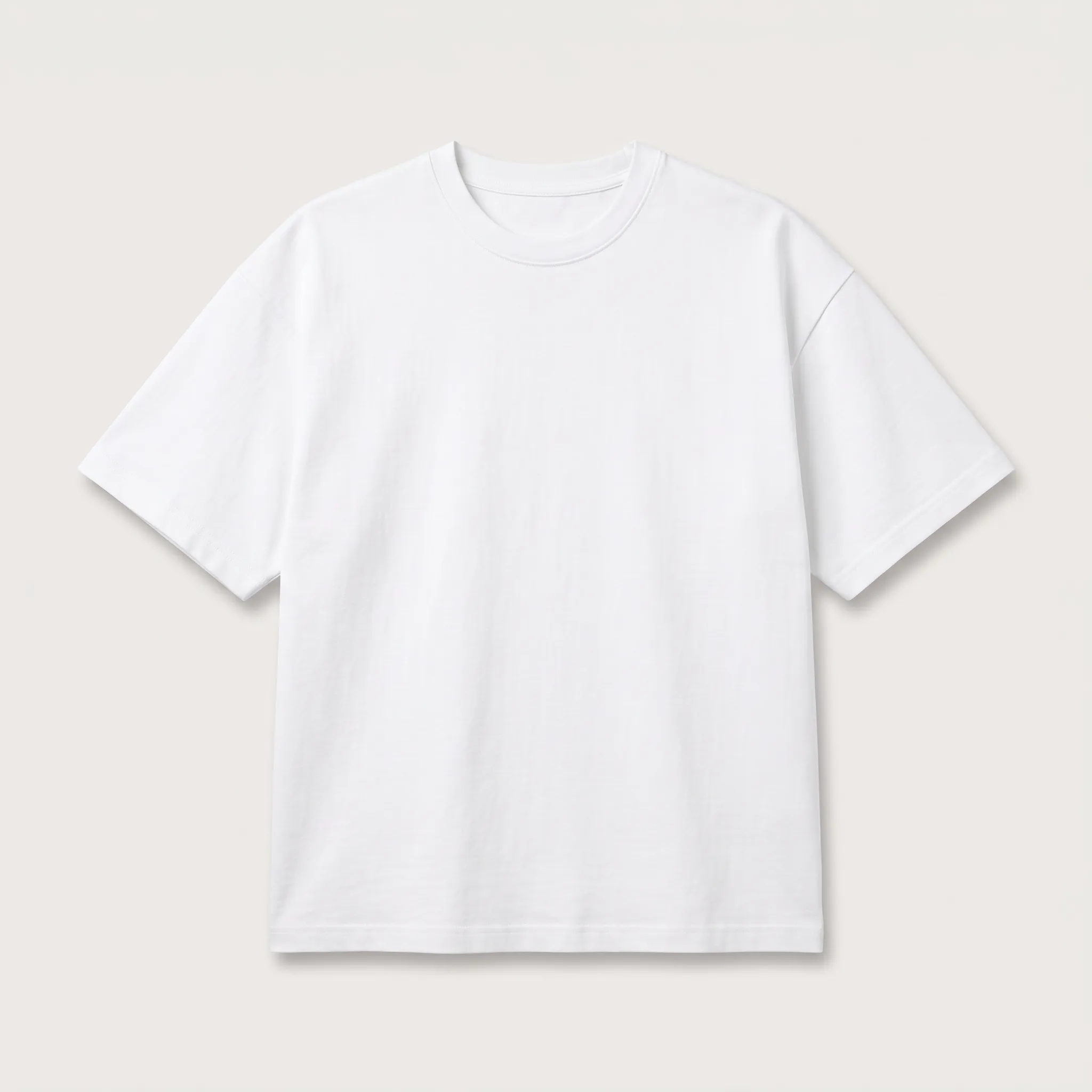 Kaos oversize lengan pendek berwarna putih polos dengan potongan badan yang longgar dan lebar serta garis bahu yang turun, menunjukkan tren fashion kasual saat ini.