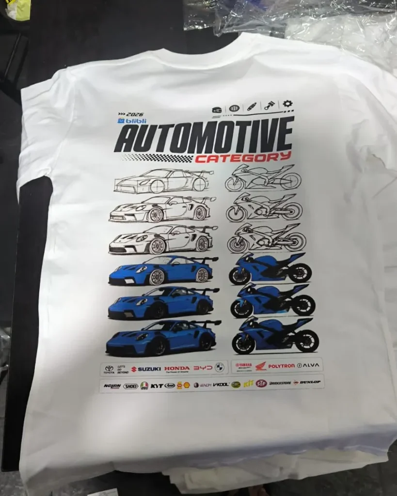 Bagian belakang kaos katun putih dengan cetakan grafis jajaran mobil sport dan sepeda motor balap bertuliskan "2026 AUTOMOTIVE CATEGORY" serta logo brand kendaraan.