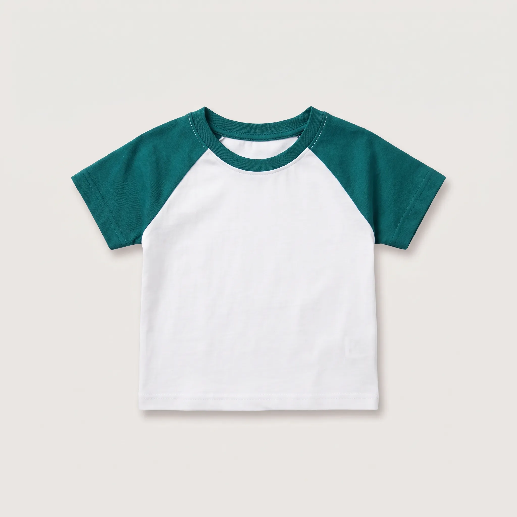 Tampilan depan kaos model raglan untuk anak-anak dengan badan berwarna putih polos dan lengan pendek berwarna hijau teal, menampilkan kerah bulat dengan jahitan tepi.