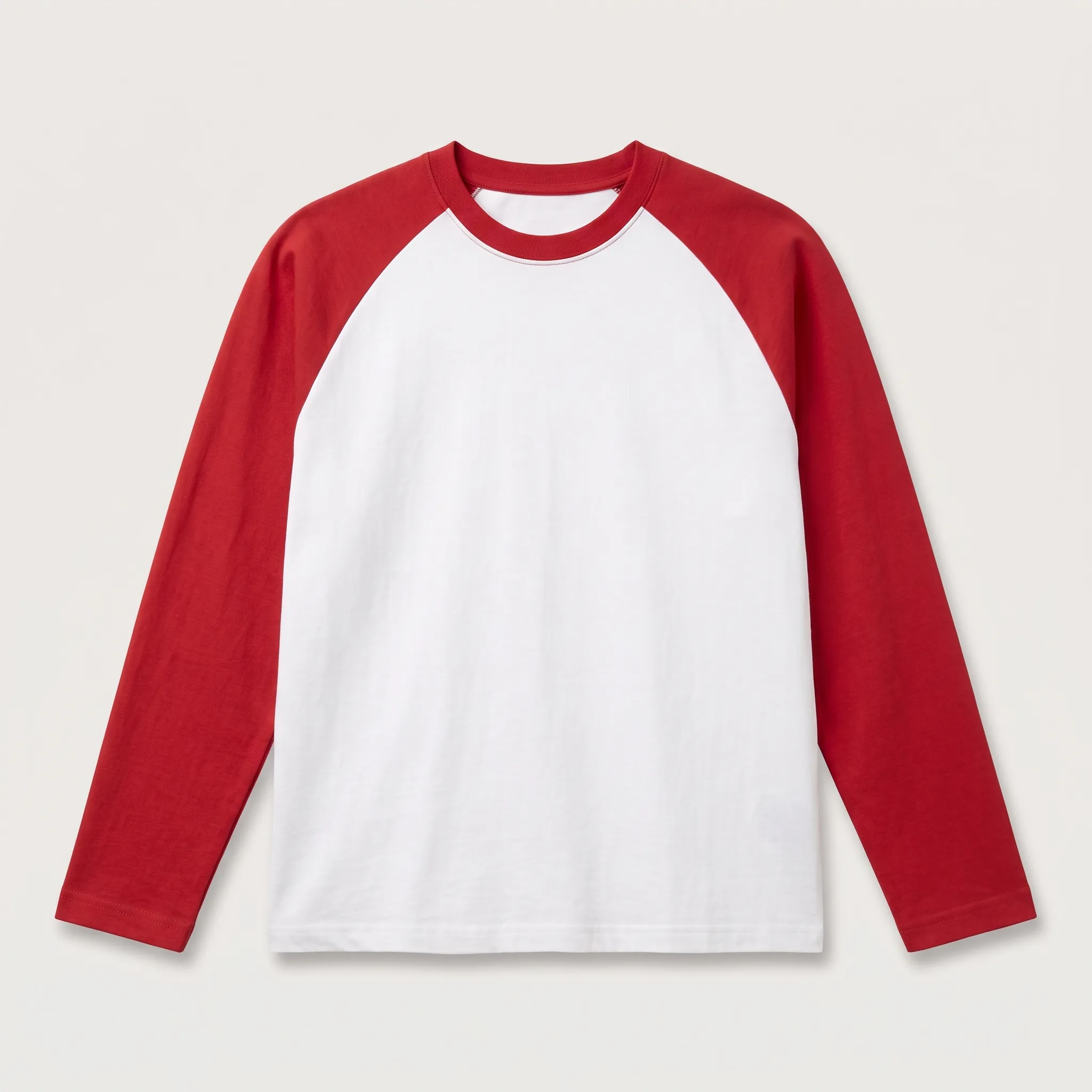 Kaos polos model raglan lengan panjang dengan perpaduan warna lengan merah dan badan putih, diletakkan mendatar di atas latar belakang abu-abu muda netral.