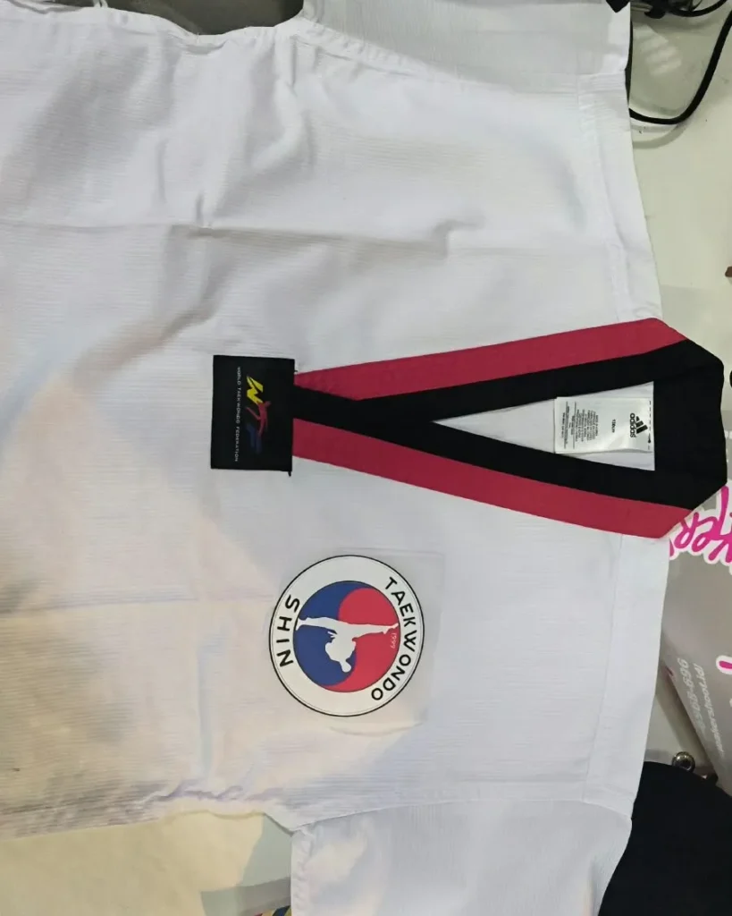 Atasan seragam martial art/taekwondo (dobok) berwarna putih merk Adidas dengan kerah kombinasi hitam-merah dan logo WTF (World Taekwondo Federation).