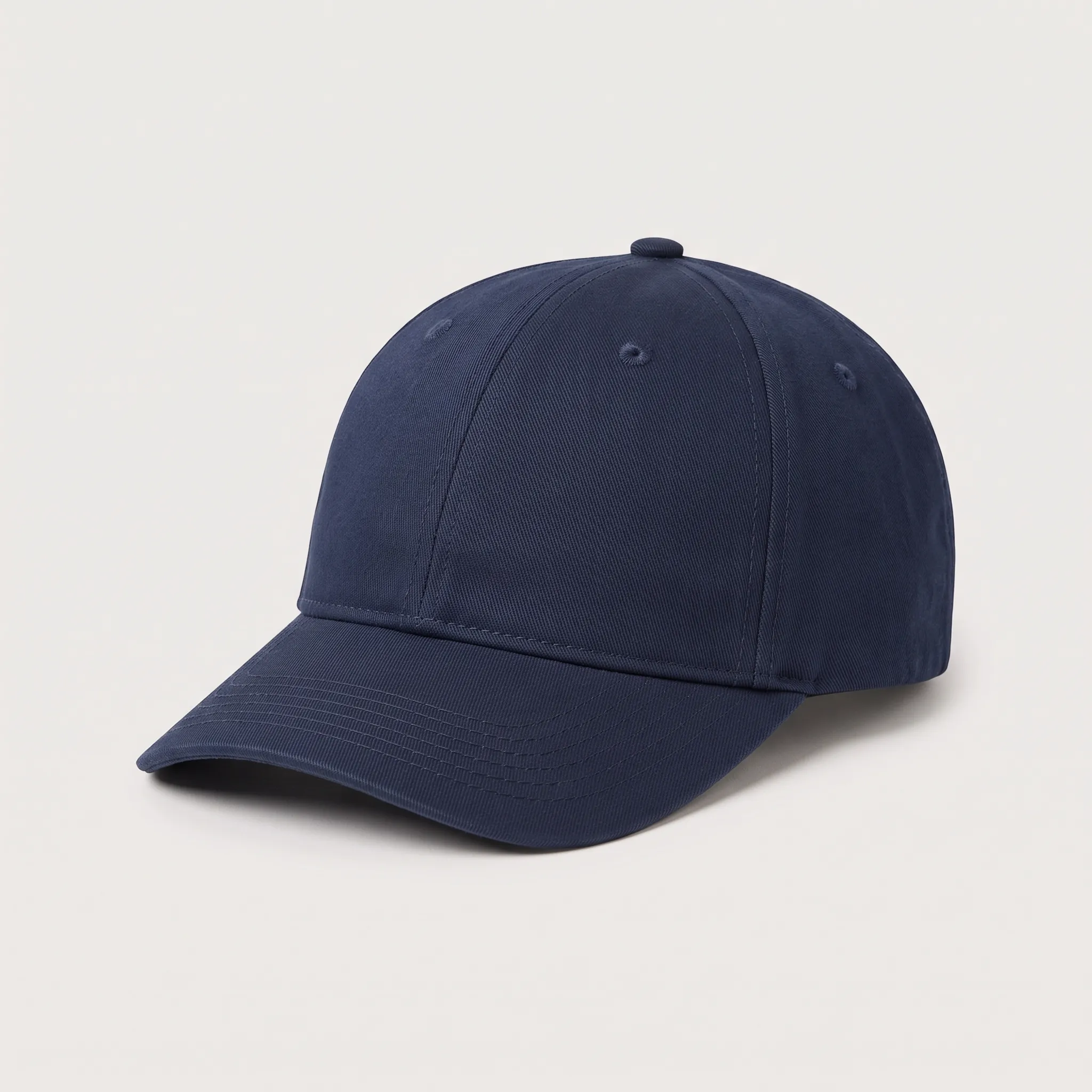 Sebuah topi baseball model klasik enam panel berwarna biru dongker polos dilihat dari sudut tiga perempat depan, menampilkan lidah topi melengkung, kancing atas, dan lubang ventilasi.